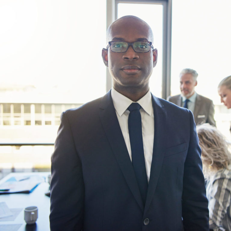 Black businessman standing in front of team looking serious and positive
